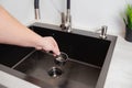 A man& x27;s hand removes a metal strainer from a kitchen sink drain. Cleaning the drain and pipes from clogging with