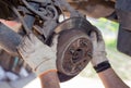 The man& x27;s hands remove the worn brake disc from the rear wheel hub.