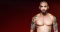 Man with beautiful muscular body with tattoos stands on red dark background and looks directly into camera Royalty Free Stock Photo