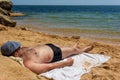 A man 30 - 40 years old in a cap, swimming trunks and sunglasses lying sunbathing on a sandy beach and looking at the sea on a hot Royalty Free Stock Photo