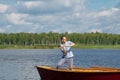 A man in yellow glasses, in a boat, in the center of the lake, throws a fishing pole to catch a big fish, against the backdrop of Royalty Free Stock Photo