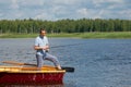 A man in yellow glasses, in a boat with oars, in the center of the lake, holds a fishing pole to catch a big fish, there is a Royalty Free Stock Photo