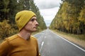 Man in a yellow hat and a sweater on a road along a golden forest. Concept of autumn mood, walking, travel and hiking Royalty Free Stock Photo