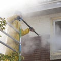 Man in yellow rain suit cleans paint from brick wall of house fa