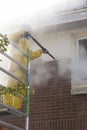 Man in yellow rain suit cleans paint from brick wall of house fa