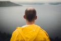 Man in yellow raincoat traveling on cliff and looking at lake in rainy windy day. Atmospheric moment. Wanderlust and travel