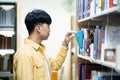 A man in a yellow shirt is looking at a book on a library shelf Royalty Free Stock Photo