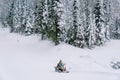 Man in a yellow ski suit rides a snowmobile through a snowy forest at the foot of a hill