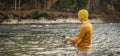 Man in a yellow sweater and hat is fishing on the river bank in the autumn forest with a spinning rod in his hands Royalty Free Stock Photo