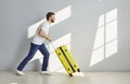 Man with a yellow travelling suitcase walking along a grey copy space wall background