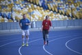Man and young disabled woman with the prosthetic leg running on the track of the stadium, evening light