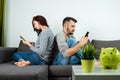 A man and a young woman, sitting on the couch and holding smartphones in their hands, turned away from each other. The concept of Royalty Free Stock Photo