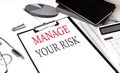 MANAGE YOUR RISK text on paper clipboard with chart and notebook on withe background