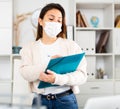 Manager girl stands in a protective mask in the office and fills out documents on a folder Royalty Free Stock Photo