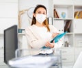 Manager girl stands in a protective mask in the office and fills out documents on a folder Royalty Free Stock Photo