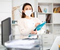 Manager girl stands in a protective mask in the office and fills out documents on a folder Royalty Free Stock Photo