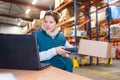 Manager scanning box while typing on laptop in warehouse