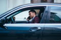 A manager sitting at the front seat of his limo talking on his cellphone while making a lot of hand gestures