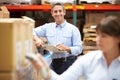 Manager In Warehouse With Worker Scanning Box In Foreground