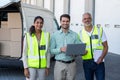 Manager and warehouse workers standing with laptop and clipboard