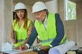 Manager watches as foreman draws pencil on drawing on table