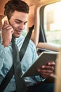 Managing business on the go. Shot of a young businessman talking on a phone while using a digital tablet in the back Royalty Free Stock Photo