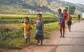 Manandoana, Madagascar - April 26, 2019: Group of unknown Malagasy kids running on road next to rice field, small hills in