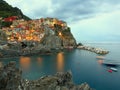 Manarola in the evening, illuminated by lampposts and by the light of the sunset with a cloud in the sky Royalty Free Stock Photo