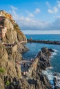 Manarola ITALY - 2 August 2023 - Construction on cliff next to the sea with people sitting on the wall at leisure