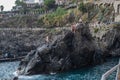 Manarola ITALY - 2 August 2023 - Teenagers rock climbing in the Mediterranean sea and girl jumping into the water