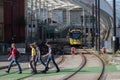 People walking across a crossing point on the tracks with yellow electric tram in the background at entrance to station Royalty Free Stock Photo