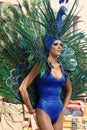 Pride parade participant dressed in blue peacock costume with colourful feathers.