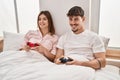 Mand and woman couple playing video game sitting on bed at bedroom Royalty Free Stock Photo