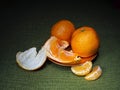 Mandarin or clementine oranges, dark still life on green. Light painting technique. Three fruit, one part peeled.