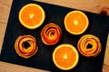 A mandarin is served on a dark stone with a decor of a peel citrus.