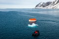 Maneuvering orange lifeboat in water in Arctic waters, Svalbard. Abandon ship drill. Lifeboat training. Man over board drill