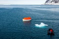Maneuvering orange lifeboat in water in Arctic waters, Svalbard. Abandon ship drill. Lifeboat training. Man over board drill