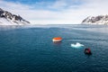 Maneuvering orange lifeboat in water in Arctic waters, Svalbard. Abandon ship drill. Lifeboat training. Man over board drill