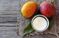 Mango body butter in a glass bowl and fresh ripe organic mango fruit and leaves on old wooden background. Royalty Free Stock Photo