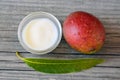 Mango body butter in a glass bowl and fresh ripe organic mango fruit and leaf on old wooden background. Royalty Free Stock Photo