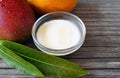 Mango body butter in a glass bowl and fresh ripe organic mango fruit and leaves on old wooden background. Royalty Free Stock Photo