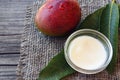 Mango body butter in a glass bowl and fresh ripe organic mango fruit and leaves on old wooden background. Royalty Free Stock Photo
