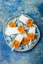 Mango passion fruit popsicles with coconut cream on ice cubes over blue plate.