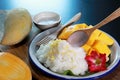 Mango sticky rice with wooden spoon pouring coconut milk in the white plate on wooden table background. Famous Dessert in Thailand