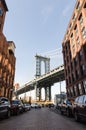 Manhattan bridge and famous alley surrounded by cars and brick buildings at Dumbo on a sunny day