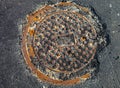Manhole with rusty metal cover in cracked asphalt surface Royalty Free Stock Photo