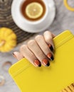 Manicured woman`s hand holding yellow notepad on gray background Royalty Free Stock Photo