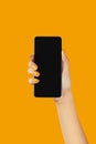 Manicured womans hand holding black smartphone with blank screen on orange background Royalty Free Stock Photo