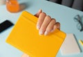 Manicured womans hand holding note pad over blue table. Back to school work from home concept