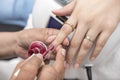 A manicurist applies a deep red gel coat nail polish onto the index fingernail and extension. At a salon or parlor